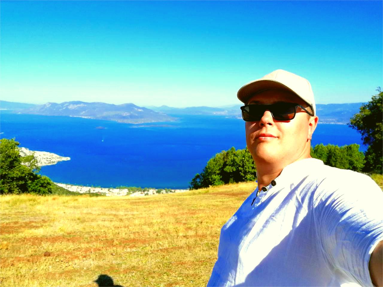 A person standing on a hill with a scenic view of the sea and mountains in the background